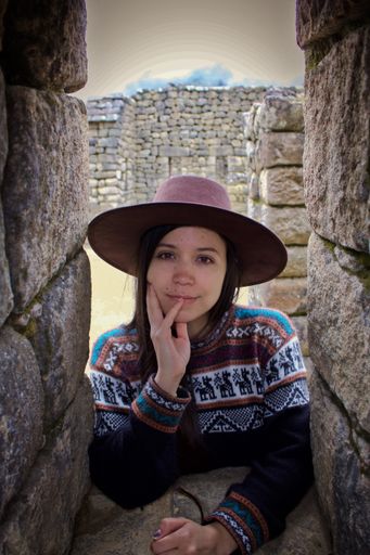 A closeup shot of a pretty Hispanic girl looking through the stone window at the lost old Inca city Machu Picchu