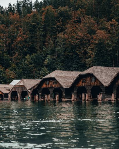 A scenic view of wooden houses on a lake against a green pine forest in Konigssee, Bavaria, Germany