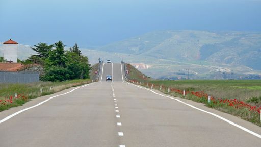 A landscape of a highway surrounded by hills and fields under a blue sky in the daylight