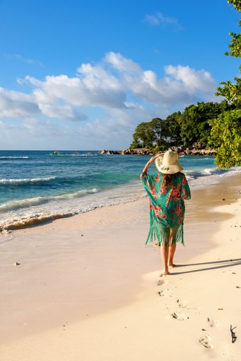 Rear view of young woman walking on idyllic tropical sandy beach on La Digue island on Seychelles.