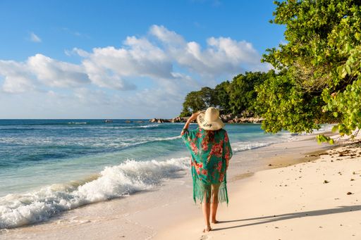 Rear view of young woman walking on idyllic tropical sandy beach on La Digue island on Seychelles.
