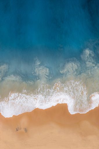 A vertical overhead shot of a wavy sea against the seashore
