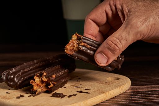 A shot of a hand holding half of a churro filled with dulce de leche and dipped in chocolate.