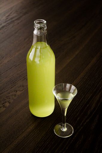 A vertical closeup of the bottle of lemon liqueur on the wooden table with a glass.