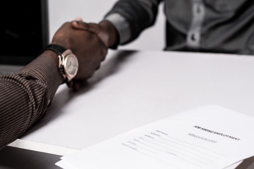 A closeup of a job application form as two black people shake hands