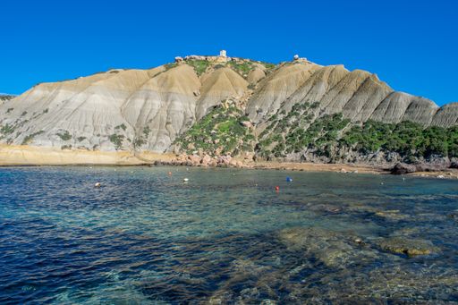 Steep blue clay slopes, with flaking debris forming scree on limestone along the coast of Xatt l-Ahmar, Ghajnsielem, Gozo, Malta, on a sunny day.