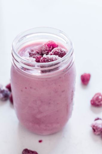 A vertical shot of a smoothie with raspberries in a glass jar