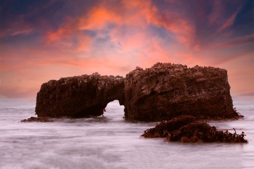 A closeup shot of a rock formation off the beach with a sunset behind it