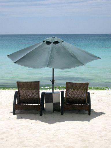 A vertical shot of  chairs under an umbrella on the beach shore with a blue sky in the background