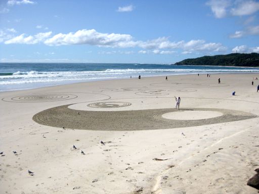 A beautiful shot of a person drawing yin and yang on the sandy surface near the water under a blue sky