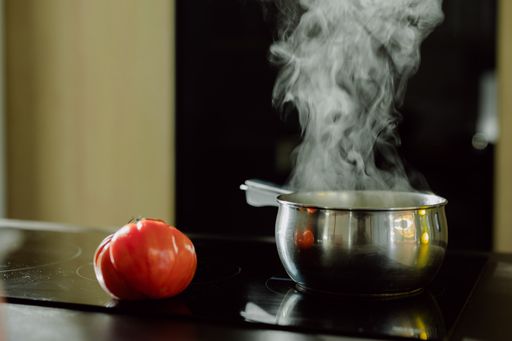 A view of the tomato near the saucepan on the electric stove with the steam coming out from it
