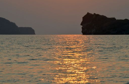A beautiful shot of a sea reflecting the sunlight with a mountain and a clear sky in the background