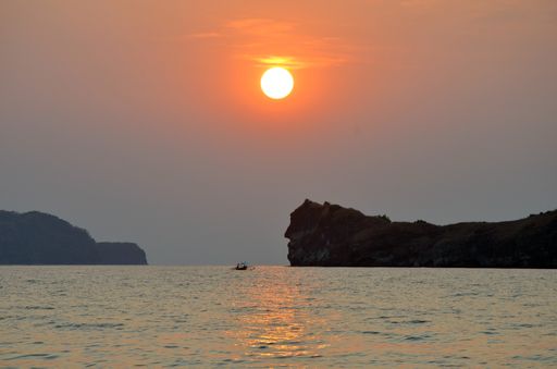 A beautiful shot of a boat on the water near a mountain under a clear sky with a red sun