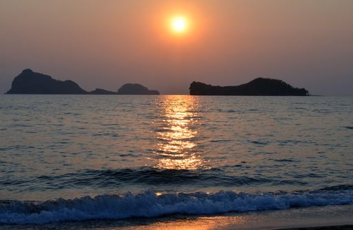 A beautiful shot of a sea reflecting the sunlight with mountains and a clear sky in the background
