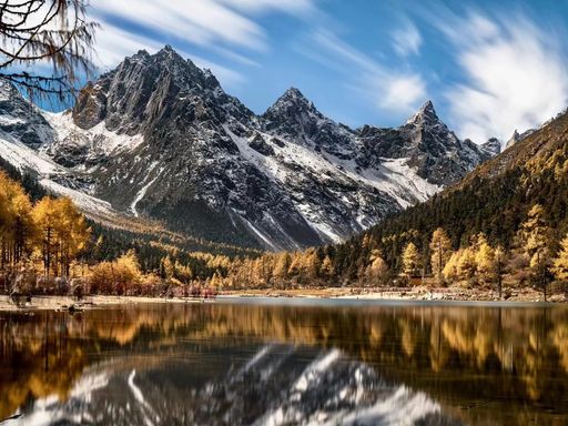 A scenic view of snowy mountains and foliage pine forests reflecting on a lake