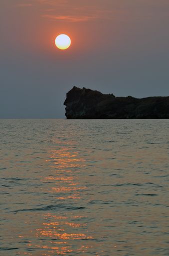 A vertical shot of a sea with a mountain and a clear sky in the background
