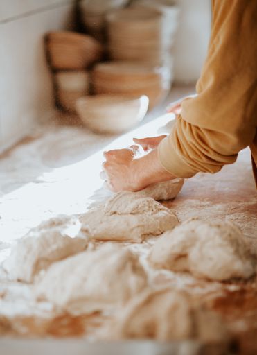 A vertical shot of a baker kneading dough on a wooden table