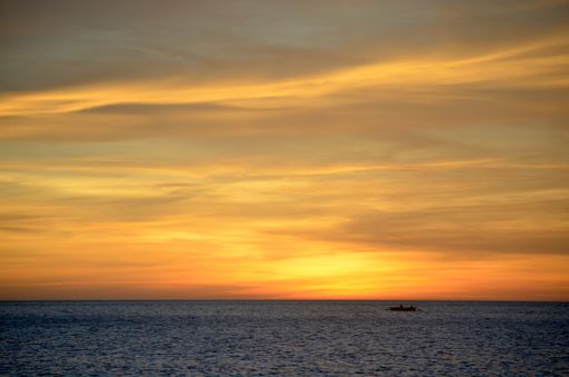 A beautiful shot of a boat sailing in the water with an orange sky in the background