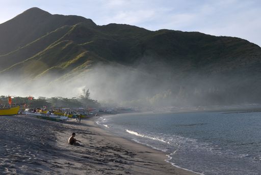 A beautiful shot of boats on the beach shore near the water with a forested mountain in the background