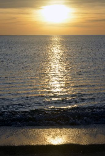 A vertical shot of sea waves reflecting the sunlight with cloudy sky in the background