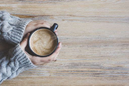 A top view of the female hands warming herself with the hot coffee on the wooden background