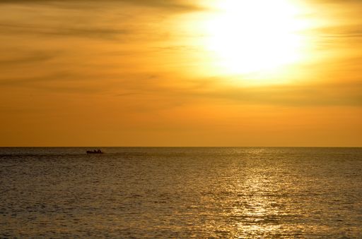 A beautiful shot of sea with a boat in the distance under a yellow cloudy sky