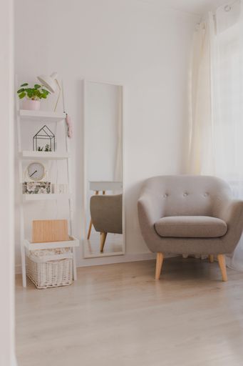 A vertical shot of a grey sofa by a vertical mirror and a shelf in a cozy room