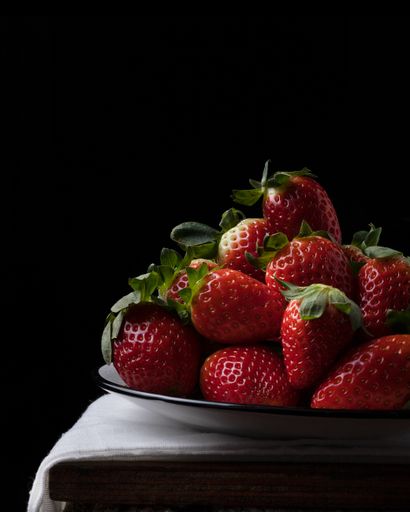 A photo of red strawberries on a black plate and a black background