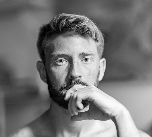 A greyscale shot of a handsome caucasian male with his hand on his chin
