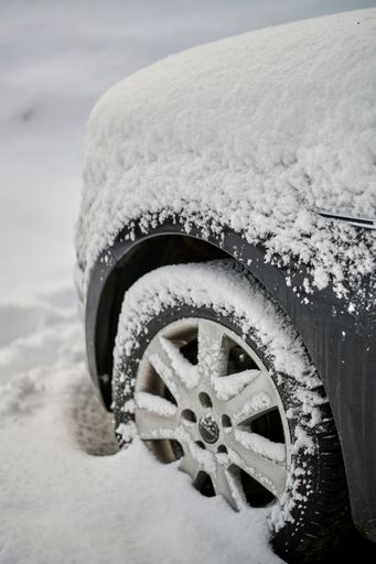 A vertical shot of a wheel of a parked car covered with snow on a cold winter day