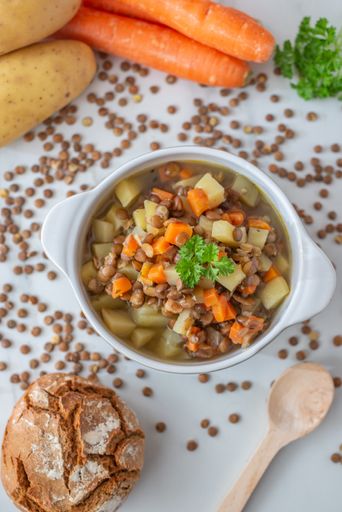 A vertical shot of a lentil soup made with veggies in a white bowl