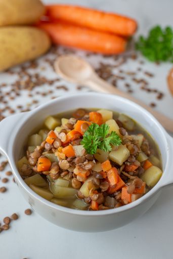 A vertical shot of a lentil soup made with veggies in a white bowl