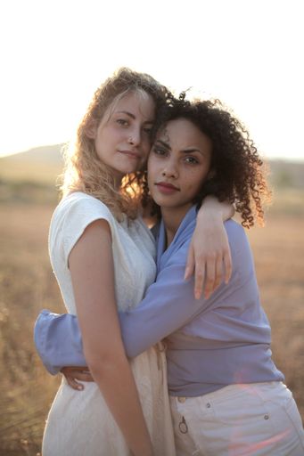A vertical shot of a blonde woman next to a curly-haired one hugging each other