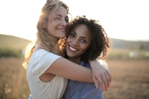 Two female friends hugging each other surrounded by a dry field