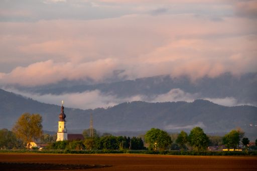 A scenic view of massive clouds over mountainous landscape with church tower