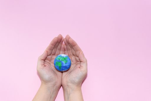 Green Energy, Renewable and Sustainable Resources. Environmental and Ecology Care Concept. Hands holding earth on pastel pink background.