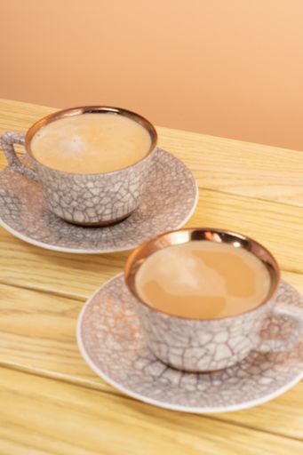 A vertical of an eastern metallic coffee cups with ornaments on a wooden table