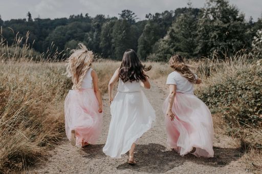 A behind shot of young girls with beautiful dresses running in the field