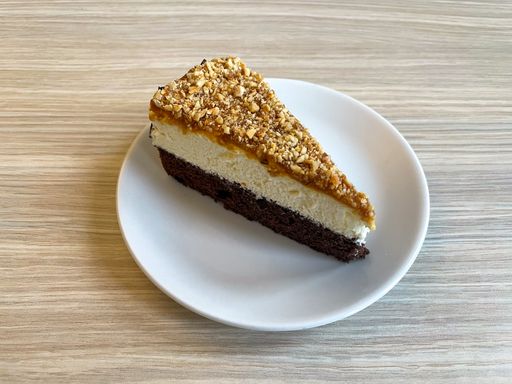 A piece of cake with a chocolate body, a layer of cream and topped with caramel nuts.