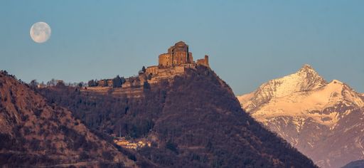The Sacra di San Michele on a huge hill in the background of a full moon.