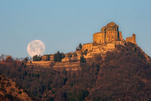 The Sacra di San Michele on a huge hill in the background of a full moon.
