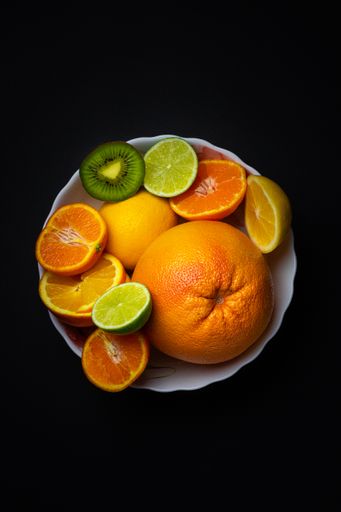 A vertical close-up top shot of citruses on a plate in the dark background.
