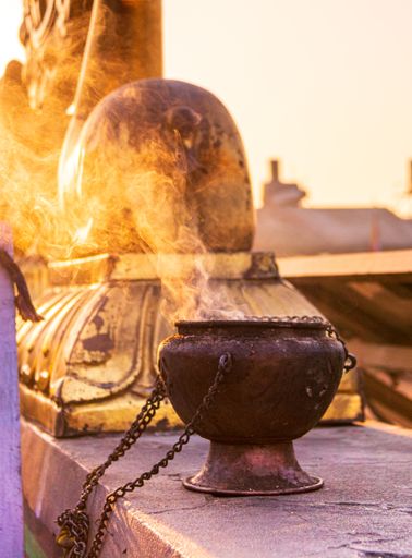 A metallic black bowl with chains put next to a statue and smoke coming out of it