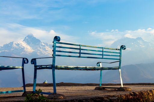 An old rusty metal bench with beautiful rocky mountains covered with snow in the background