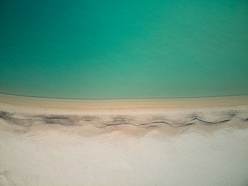 A drone shot of soft sandy beach with green water