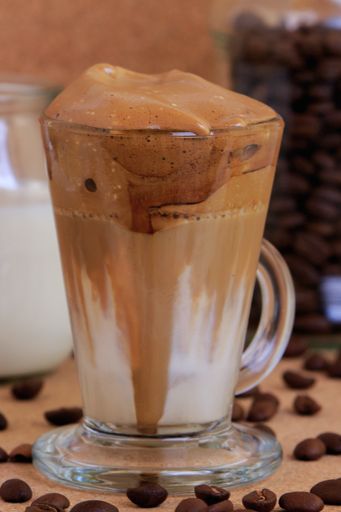 A vertical shot of a glass of fresh dalgona coffee in a coffee shop with a blurry background