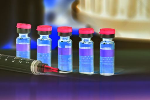 A syringe needle with vials of COVID vaccine in the laboratory in negative tones