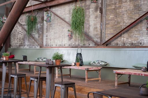 A cafe interior with chairs, tables, flowers in pots and hanging on the wires against brick wall