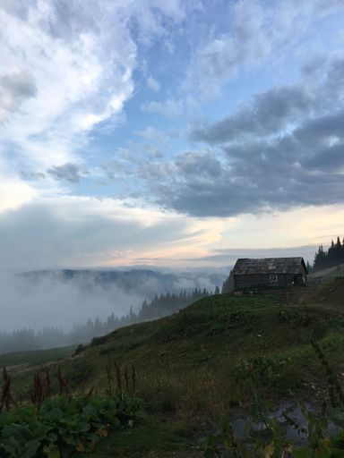 A vertical shot of a beautiful green steep hill with a small wooden house on it under a beautiful sky