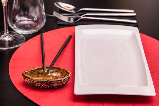 A closeup shot of a served table with a white plate, empty sauce boat and chopsticks